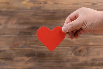 A man's hand with a red heart symbol on a wooden background, copyspace
