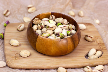 Roasted salted pistachio nuts in nutshell in wooden bowl on textured background.