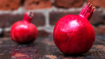 On the table lay two red pomegranate. Two ripe garnet on the table on red brick wall background....