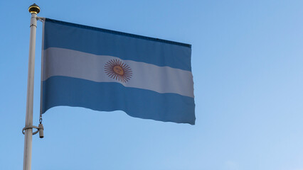 National flag of Argentina on a flagpole in front of blue sky with sun rays and lens flare. Diplomacy concept.