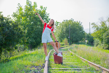 cheerful woman with a hat walks on the rails with a suitcase