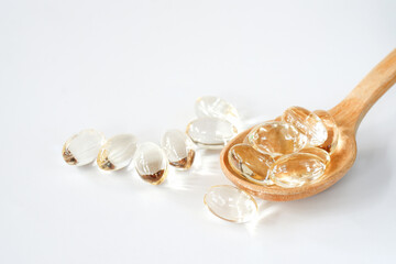 Coconut oil capsules in a wooden spoon on a white background. Health food supplement concept.