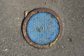 Close-up view of a small iron cover plate for a water valve on a city street