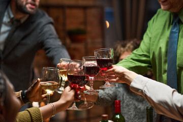 Close-up of group of people toasting glasses with red wine during a party at home