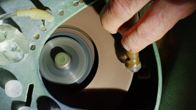 A man works in gem studio cutting and faceting stones. A worker polishes a gemstone on a faceting machine in a cutting and polishing workshop