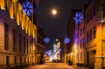 Fototapeta na wymiar Panorama of a winter evening in the city, illuminated by evening street lights, before Christmas. Snowy streets, snowflakes. Riga, Latvia.