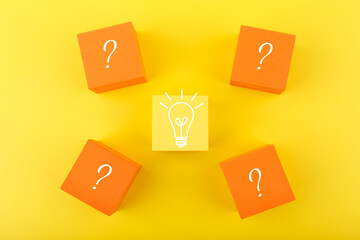 Creativity, innovation and idea concept. Flat lay with light bulb drawn on yellow cube and question signs on orange cubes