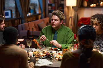 Group of friends talking to each other while having dinner at the table during a dinner party