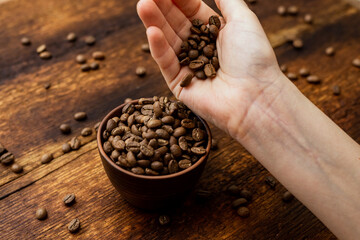 Coffee beans full cup and female hands on brown old wooden background.