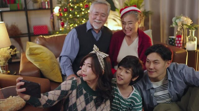 Asian multi generation family parent and grand parent sit relax smile together fun and using smartphone talking selfie photo happiness together livingroom at home during christmas thanksgiving weekend