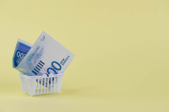 Israel Money Shekel Banknotes In Shopping Cart On Yellow Background. Exchange Rates And Buy Sell Currency Concept.