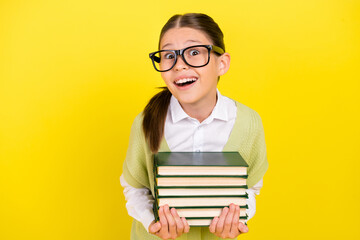 Portrait of attractive curious girlish amazed cheerful girl holding book having fun isolated over bright yellow color background