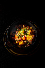 Goulash. Vegetable rague with meat, eggplant, pepper, potato and carrot in black bowl on dark wooden background
