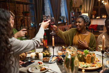 Group of friends toasting with glasses of red wine at the table during a festive dinner in the living room