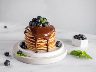 Pancakes with chocolate syrup, blueberries and mint on a marble table