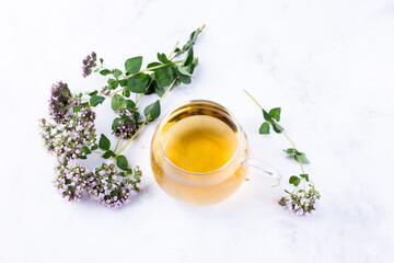 Herbal tea in a glass cup, fresh oregano flowers on a light background. Medicinal plants. The drink...