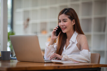 Shot of an Asian young businesswoman working on a laptop computer in her workstation.Portrait of Business people employee freelance online marketing e-commerce telemarketing concept.