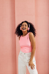 Fototapeta premium Young happy woman in casuals wearing pink headphones listening music with closed eyes