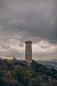 Large ancient stone tower stands on a hill in the forest. Mountain view with tragic sky. Old architecture, historical heritage, medieval tower