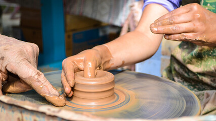 The hands of an old teacher and a young student in clay. The potter's wheel rotates the clay under the palms. Handmade, working with natural materials, hobby.