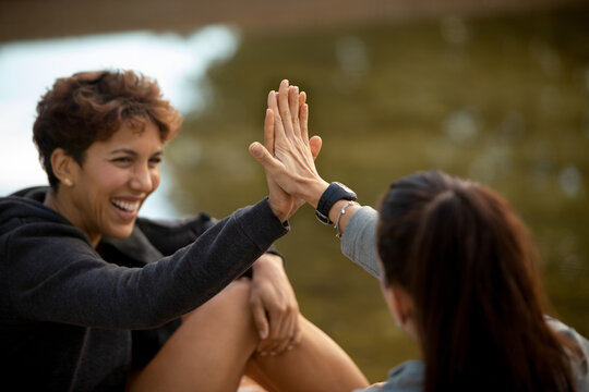 Cheerful Hispanic female giving high five to friend in park
