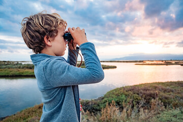 An adventurous boy explores the landscape with binoculars with the cloudy horizon, concept of...