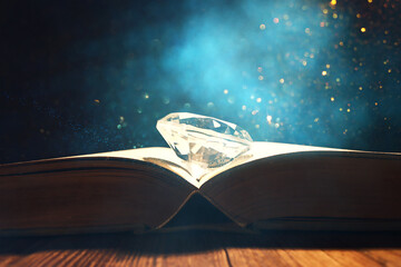 image of open antique book and diamond on wooden table with glitter overlay