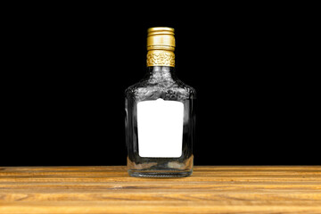 Mockup label on empty glass bottle of whiskey, cognac or vodka on a black background, wooden table....