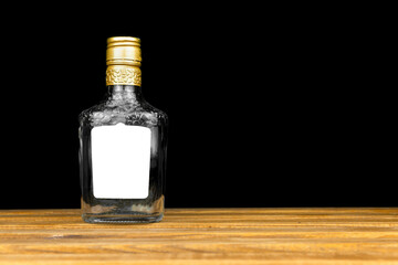 Mockup label on empty glass bottle of whiskey, cognac or vodka on a black background, wooden table....