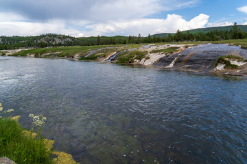 Green grass, trees, and rock line the Firehole River in Yellowstone National Park in Wyoming on a sunny summer day