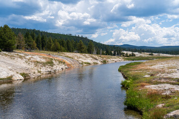 Fototapeta na wymiar Green grass, trees, and rock line the Firehole River in Yellowstone National Park in Wyoming on a sunny summer day
