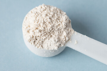 Top view of diatomaceous earth or diatomite powder in a plastic spoon on a blue background. Close up of white powder in a scoop