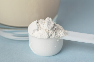 Preparation of the detox drink with mineral supplement diatomaceous earth or diatomite powder in a plastic spoon. White powder in a scoop and glass of water blue background
