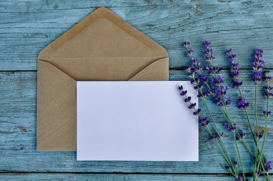 Mockup of craft paper envelope with blank white card  with lavender flowers on blue old wooden background close-up. Happy Birthday, Valentine's day, wedding, Mother's Day greeting,  invitation card.