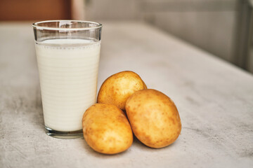 A transparent glass with potato milk on the table next to the potato tubers. 