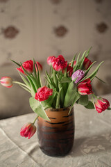 Naklejka na ściany i meble Spring flowers in vase on table. Beautiful spring tulips in vase on table against light background.