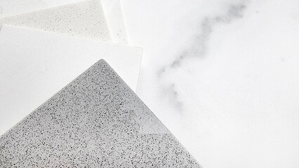 close up top view of stacked artificial stone sample swatches in light tone placed on ceramic white carrara marbled tile with blank space for design. focused at grainy grey stone textured.