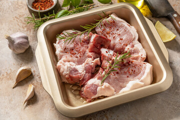 Fresh raw pork loin on the bone with spices and marinade on a stone tabletop, preparation for baking or barbecue.