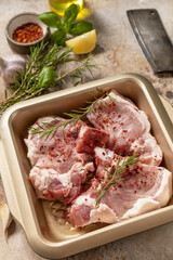 Fresh raw pork loin on the bone with spices and marinade on a stone tabletop, preparation for baking or barbecue.
