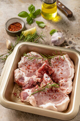 Fresh raw pork loin on the bone with spices and marinade on a stone tabletop, preparation for baking or barbecue.