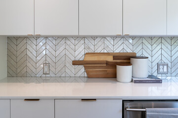 Modern kitchen detail of chevron pattern silver tile backsplash with sleek white countertop and white cabinets.