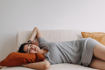 Obraz premium Asian woman in grey dress is sleeping and relaxed on the sofa in the apartment.