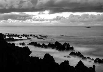 Porto Moniz on coast of Madeira island Portugal with dark lava rocks and islands near shore. Dusk...