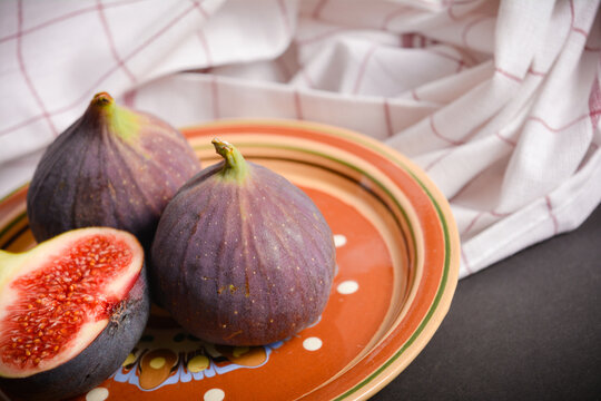 Close up of Azerbaijani fig fruit with almonds. Exotic eastern fruit cut. Segmented berry served on clay plate painted in ethnic style on black background with kitchen textile towel. Text space image
