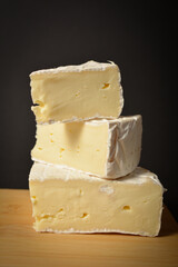 Side view of Cheeseboard with soft French Brie cheese pieces served on wooden board on dark background. Three pieces of cheese with. Healthy Starter, appetizer, snack or dessert
