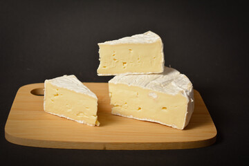 Cheeseboard of soft French Brie cheese pieces on wooden board on dark background. Three pieces of cheese 
