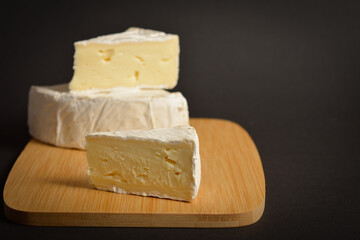 Cheeseboard of soft French Brie cheese pieces on wooden board on dark background. Three pieces of cheese 
