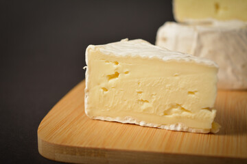 Close up of soft French Brie cheese pieces on wooden board on dark background. Cheeseboard of Three pieces of cheese
