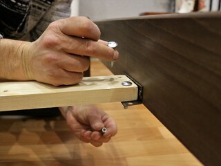 inserting bolts into the hole of the plank when assembling the base of a wooden bed, connecting and fixing parts of the furniture structure, fasteners for fixing the base of the bed in the hands