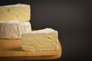 Close up of soft French Brie cheese piece on wooden board on dark background. Cheeseboard of platter of Three pieces of cheese
